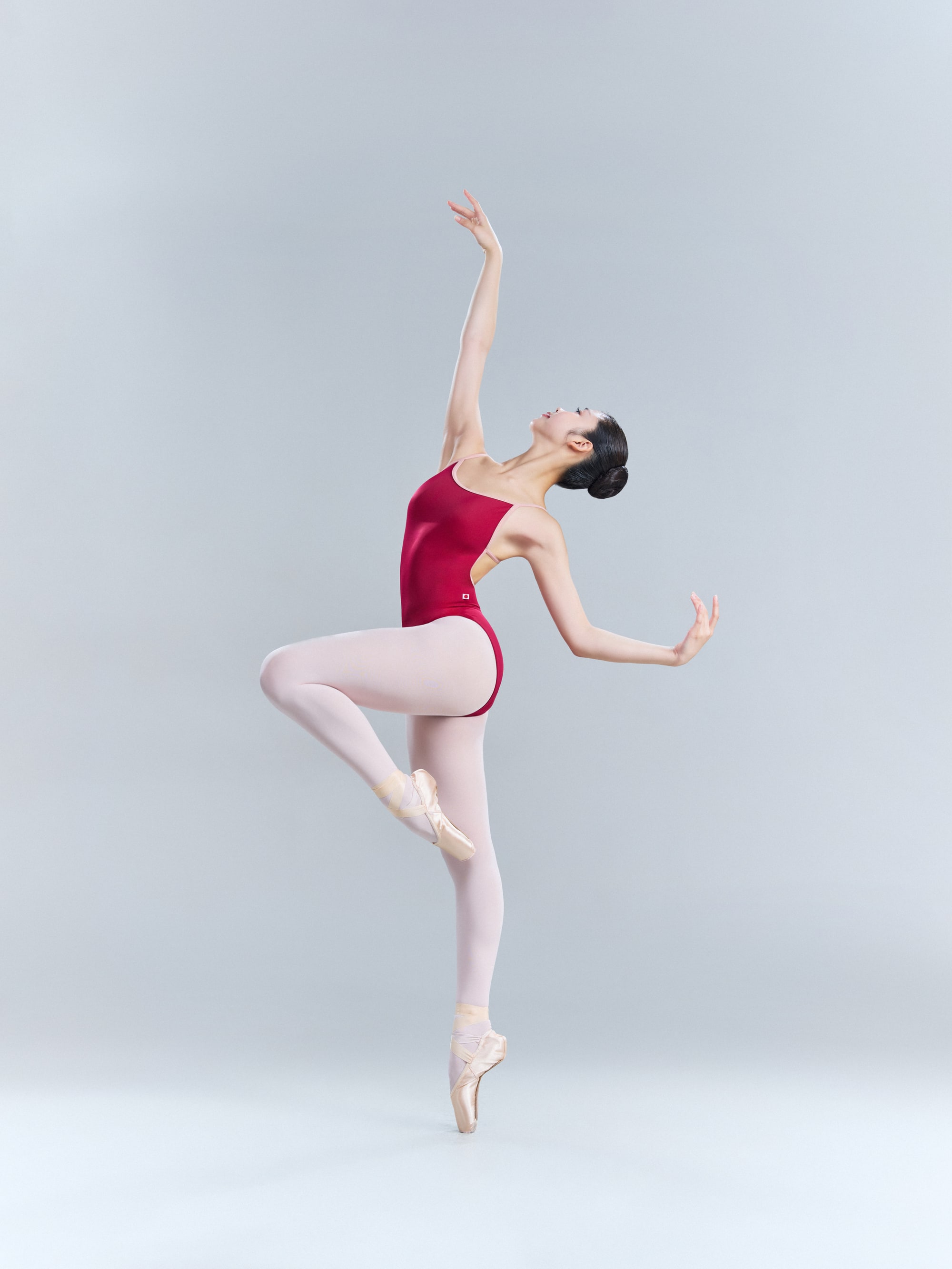 Attitude derrière en pointe in a red leotard, arm raised