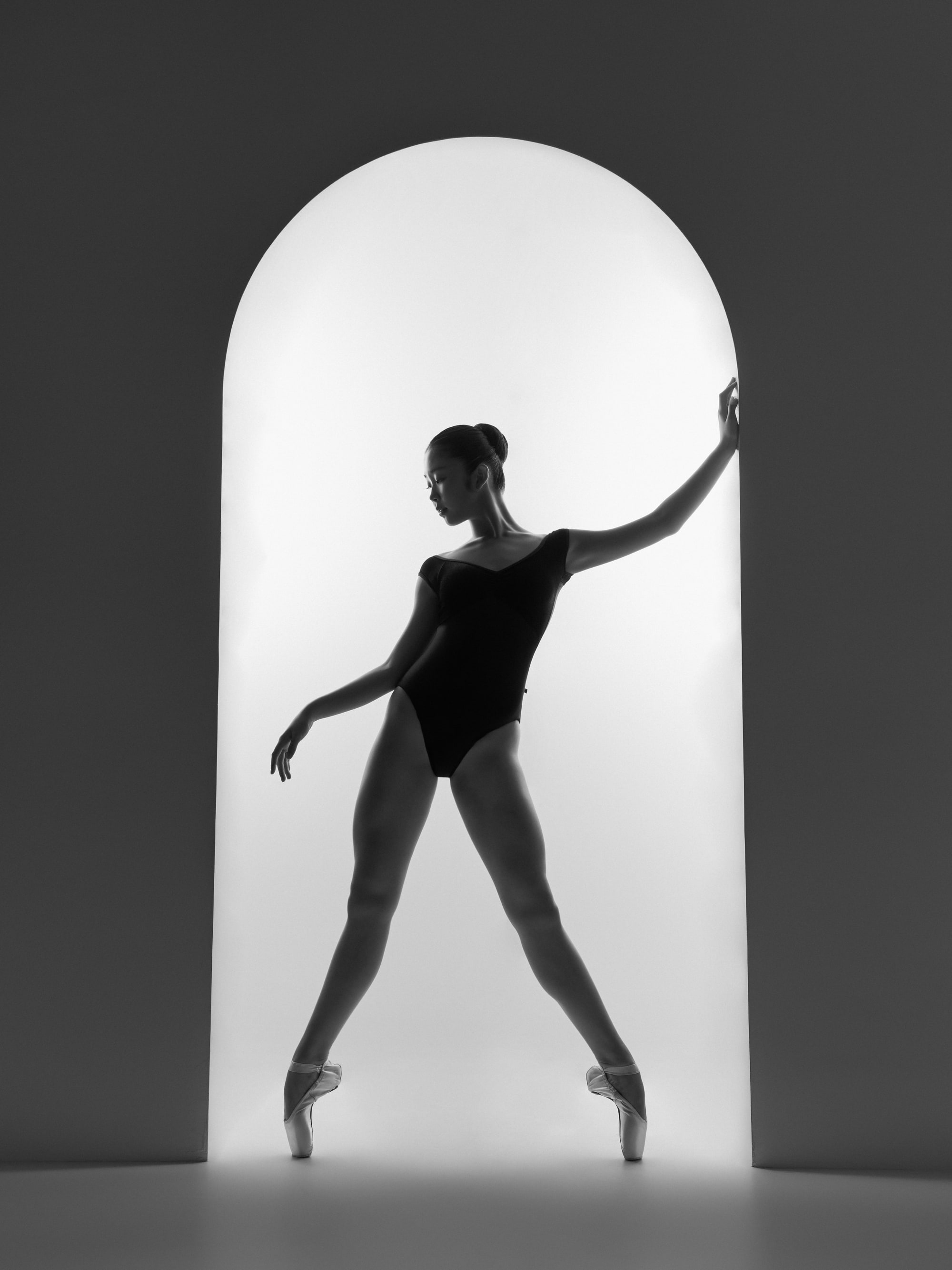 Silhouette in an arched doorway, tendu with one hand on the arch