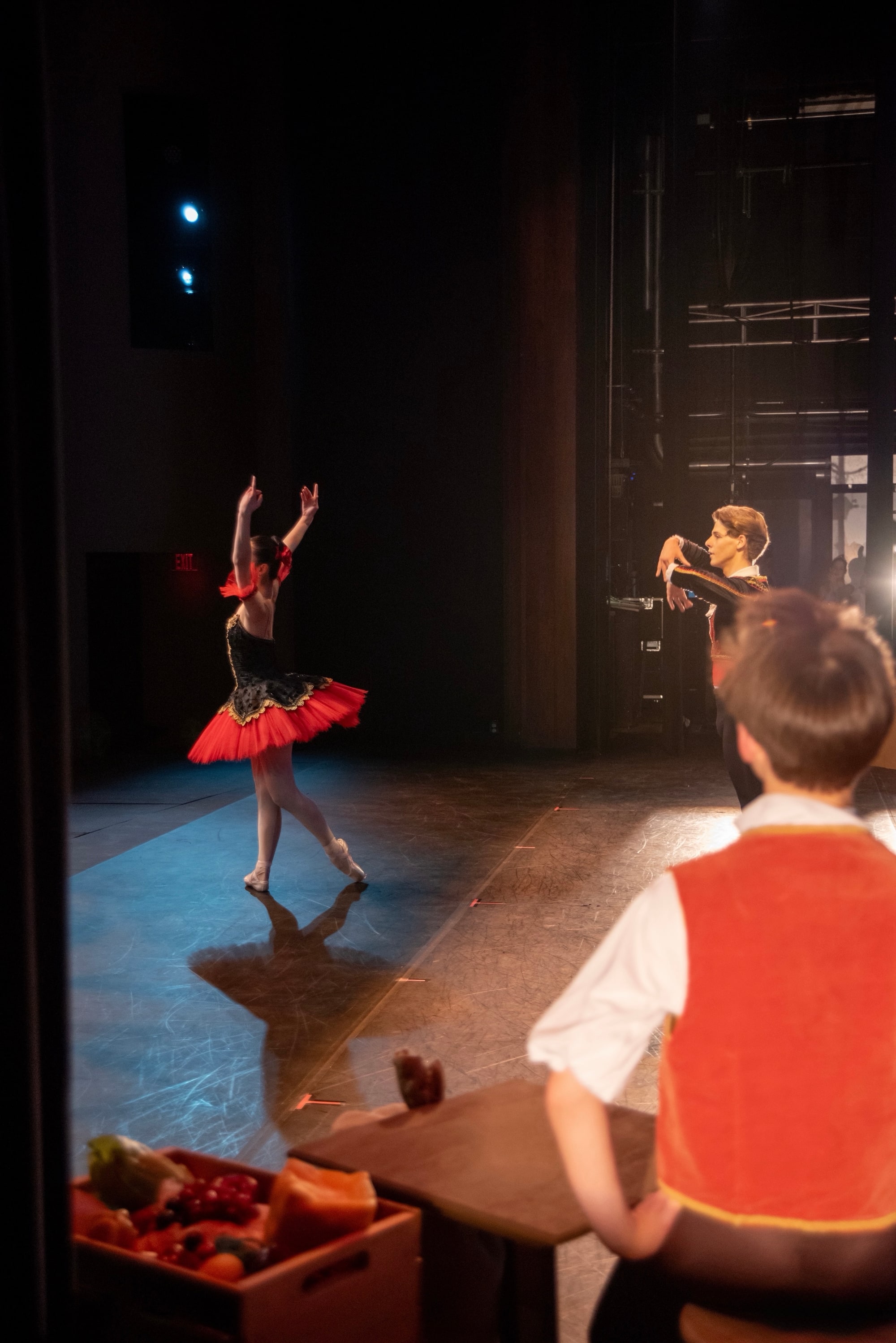 Kitri seen from the wings, arms raised, with Basilio upstage